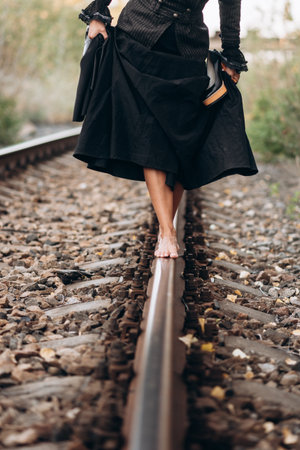 Barefoot Woman Balances on Railway Track in Black Dressの写真素材