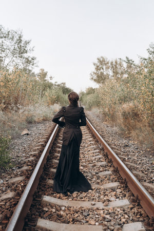 Woman in Black Dress Walking on Railroad Tracks at Duskの写真素材