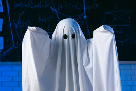 A person in a white ghost sheet stands in a blue-lit room and makes a frightening gesture