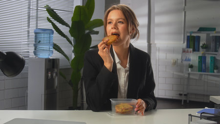 Businesswoman Enjoying a Snack Break in Modern Officeの写真素材