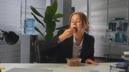 Woman Enjoying Noodles in an Office Setting during a Casual Lunch Breakの写真素材