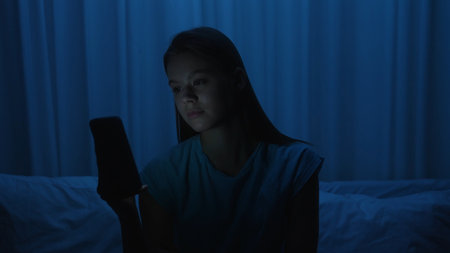 A young woman uses a smartphone in bed at night