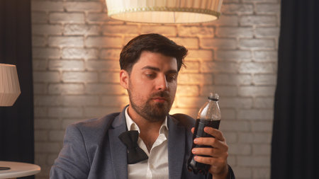 A businessman in a business suit drinks soda from a plastic bottle in a modern room with ambient lighting. An office worker relaxes during lunch.の写真素材