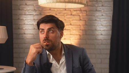 A businessman in a suit enjoys delicious French fries in a cozy cafe. An office worker relaxes and eats fast food during his lunch break.の写真素材