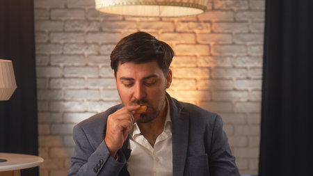 A businessman in a suit enjoys delicious chicken nuggets in a cozy cafe. An office worker relaxes and eats fast food during his lunch break.の写真素材