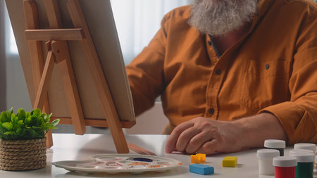 An elderly male artist paints at home using a wooden easel. The scene captures artistic creativity.の写真素材