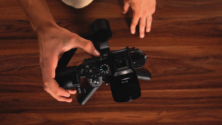 Top shot at hands adjusting a digital camera mounted on a gimbal over a wooden surface, emphasizing control and precision.の写真素材