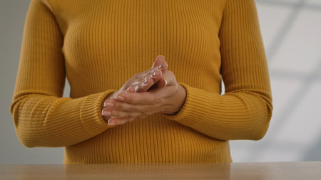 Close up shot of a person wearing a yellow ribbed sweater, with hands resting on a table.