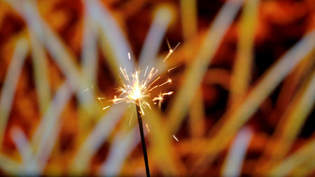 Close up of Bengal fire burning with bright golden sparks against the backdrop of bokeh fireworks....