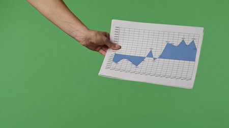 A woman hand holding a economic graphs on a green chroma key background. Shot for designs related to office, business, startup, economy, and stock market.の写真素材