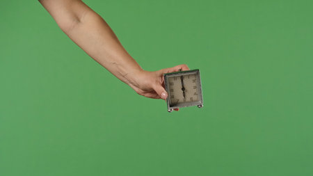 A woman hand holding a vintage table clock on a green background. Shot for designs related to...