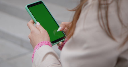 Close up of a person holding a smartphone with a green screen, ideal for mockups or presentations.