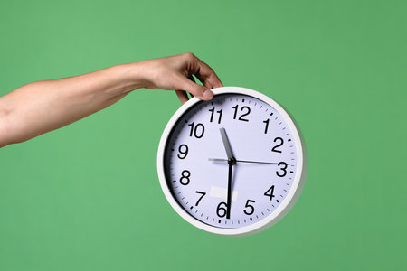 A woman hand holding a clock on a green chromakey background. Shot for designs related to office,...