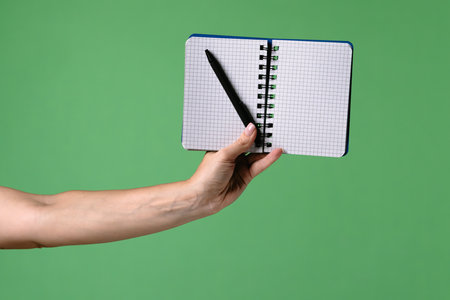 A woman hand holding an open notebook and pen on a green chroma key background. Shot for designs related to office, business, education and training.の写真素材