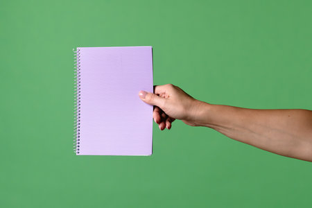 A woman hand holding a purple notebook on a green chroma key background. Shot for designs related to...