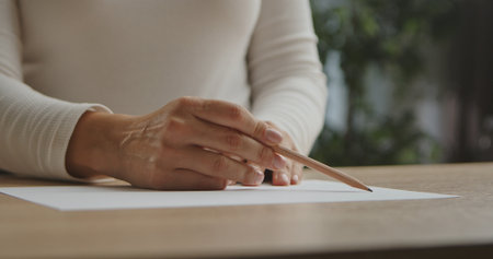 A close up image of a woman hand holding a pencil and writing on a blank sheet of paper.の写真素材