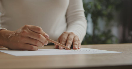 Close up of woman hands drawing on paper with a pencil on a wooden desk, showcasing creativity and focus.の写真素材