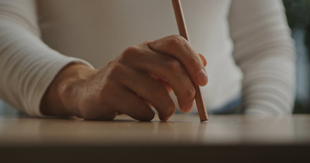 A detailed view of a hand poised with a pencil, ready to write or draw on a smooth wooden surface.の写真素材