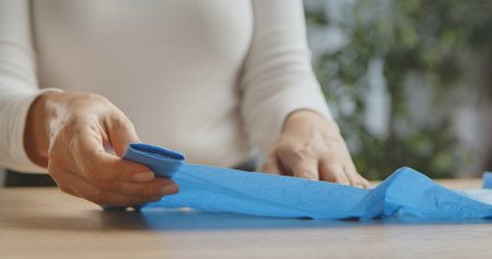 A close up image of hands carefully folding a blue plastic bag on a wooden table, with a soft background.の写真素材