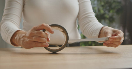 A close up view of woman hands skillfully handling clear adhesive tape on a wooden table surface.の写真素材