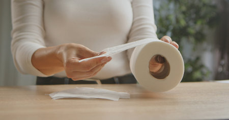 Close up of woman hands holding a toilet paper roll above a wooden table, emphasizing hygiene and daily essentials.の写真素材