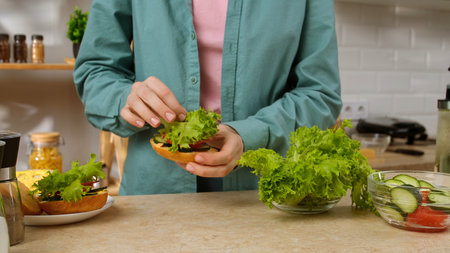 Close up of hands making a sandwich with fresh lettuce and vegetables. Preparing a healthy breakfast or snack in the kitchen at home.の写真素材