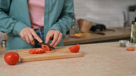 Close up of hands slicing a fresh tomato on a wooden cutting board. Preparing a healthy breakfast or...