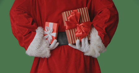 A rear view of Santa in a red suit holding gift boxes with red bows on a green background,...