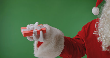 Santa Claus in a red suit with a white fur cuff and glove holding a gift box against a green background. Perfect for Christmas banners, cards, and holiday advertising.の写真素材