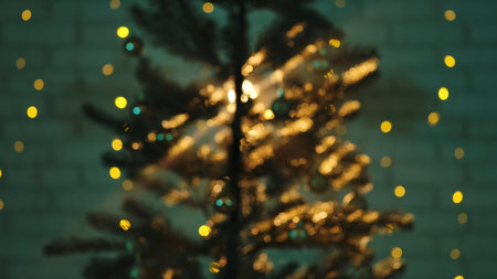 A blurred image of a Christmas tree illuminated by golden bokeh lights, creating a warm and festive ambiance. Background for New Year holiday screensavers.の写真素材