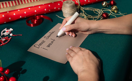 Top view of female hands writing a Christmas letter that begins Dear Santa, I want on a piece of...