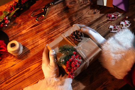 Top view of Santa Clauss gloved hands creating festive gifts with his own hands on a rustic wooden table. Preparing for New Years and Christmas celebrations.の写真素材