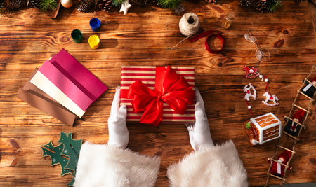 Top view of Santa Clauss gloved hands creating festive gifts with his own hands on a rustic wooden table. Preparing for New Years and Christmas celebrations.の写真素材