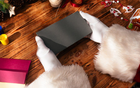 Top view of Santa's gloved hands selecting colored cardboard to make Christmas cards on a rustic wooden table with ribbons, stamps, and a wrapped gift. Festive scene for crafts.の写真素材