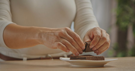 Close up of hands breaking crispy chocolate wafers onto a white plate, demonstrating how to make a homemade dessert.の写真素材