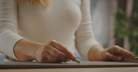 A close up view of a woman hand holding a piece of chalk, poised to write on a chalkboard.