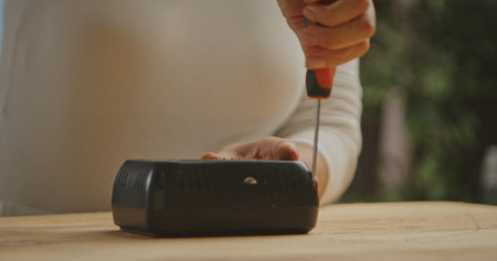 Close up of a woman, hand using a screwdriver on a black electronic device on a wooden surface.の写真素材