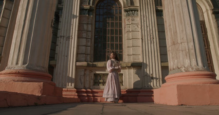 A woman in long dress standing in front of the massive viewing doors of an old building with columns.の写真素材