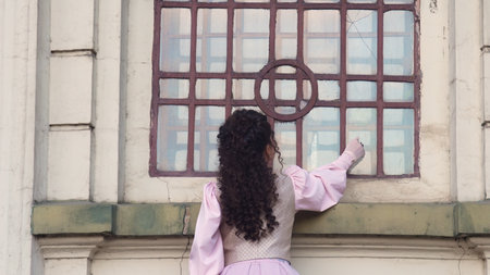 A woman in an elegant historical dress reaches out her hand to the antique window of an old cathedral, symbolizing memory, longing, and connection to the past.の写真素材