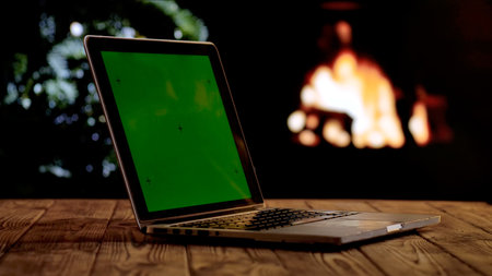 Laptop with a green screen chroma key screen against a glowing fireplace and Christmas tree. A warm, festive atmosphere for digital or themed layouts.の写真素材