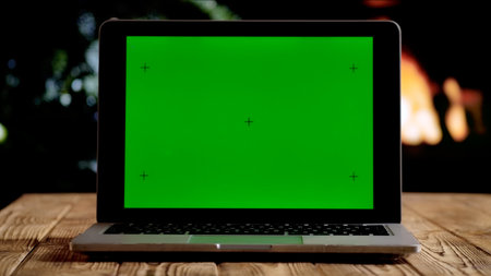 Laptop with a green screen chroma key screen against a glowing fireplace and Christmas tree. A warm, festive atmosphere for digital or themed layouts.の写真素材