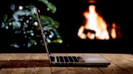 Laptop against a glowing fireplace and Christmas tree. Freelancing, remote work, or studying at home during the holidays. A warm festive atmosphere for New Year or Christmas.の写真素材