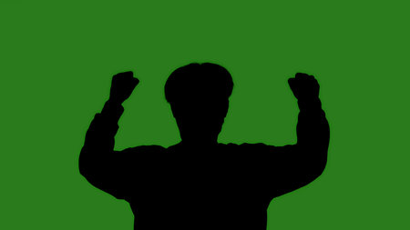 An isolated black silhouette of a man raising his hands in a protest against a green chroma key background. Minimalistic contrast and modern visual composition, mockup.の写真素材