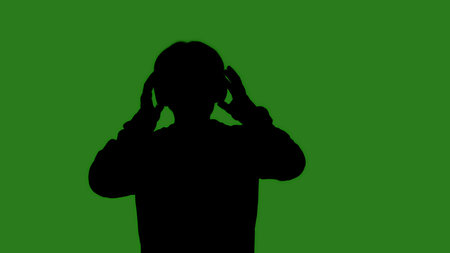 An isolated black silhouette of a man putting on headphones against a green chroma key background. Minimalistic contrast and modern visual composition, mockup.の写真素材