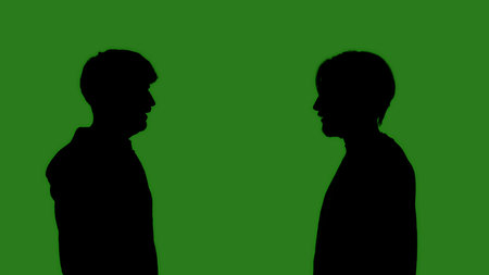 Black silhouettes of two men looking at each other against a green chroma key background. Minimalist contrast and modern visual composition, mockup.の写真素材