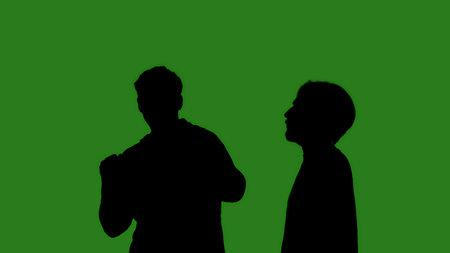 Black isolated silhouettes of two men dancing cheerfully on a green chroma key background. Minimalist contrast and modern visual composition, mockup.の写真素材