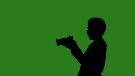 Black isolated silhouette of a man with a camera on a green chroma key background. Minimalist...