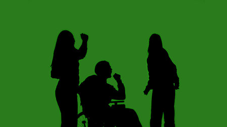 Black isolated silhouettes of people and individuals in wheelchairs dancing cheerfully on a green chroma key background. Minimalist contrast and modern visual composition, mockup.の写真素材
