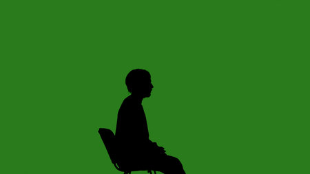 A black silhouette of a man sits on a chair and thinks about something against a green chroma key background. Minimalist contrast and modern visual composition, mockup.の写真素材