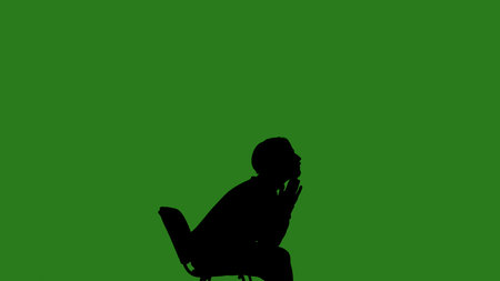 A black silhouette of a man sits on a chair and thinks about something against a green chroma key background. Minimalist contrast and modern visual composition, mockup.の写真素材